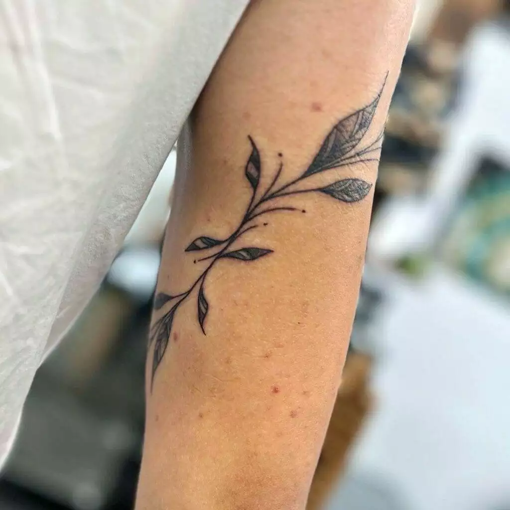 A black and white tattoo of a leaf on the arm.