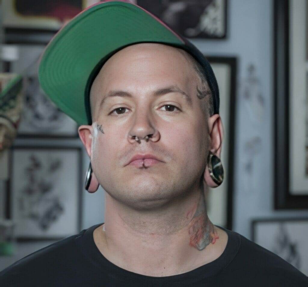 A man in a green hat with tattoos on his face walks into a tattoo shop in San Diego, known for offering the best tattoos.