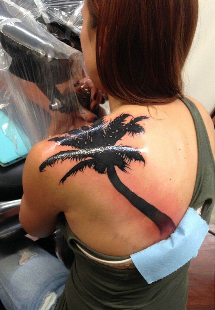 A woman is getting a tattoo of a palm tree on her back.