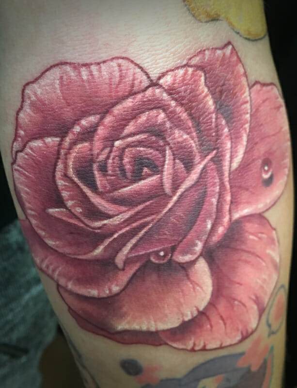 A tattoo of a pink rose on a person's forearm.