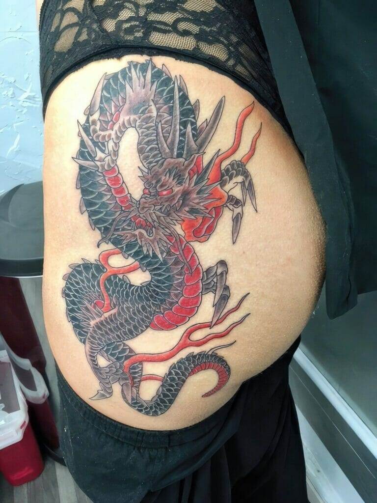 A black and red dragon tattoo on a woman's thigh.