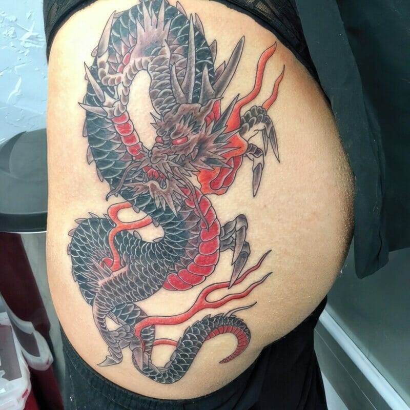 A black and red dragon tattoo on a woman's thigh.