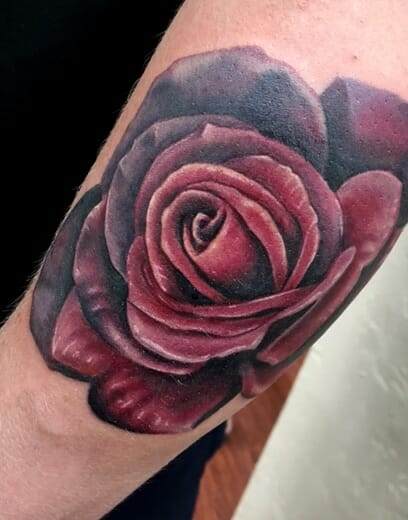 A burgundy rose tattoo on the forearm.