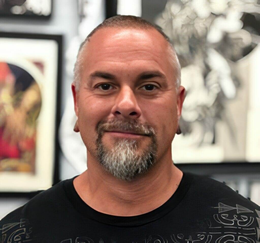 A tattooed man standing in front of a wall of art at the best tattoo shop in San Diego.