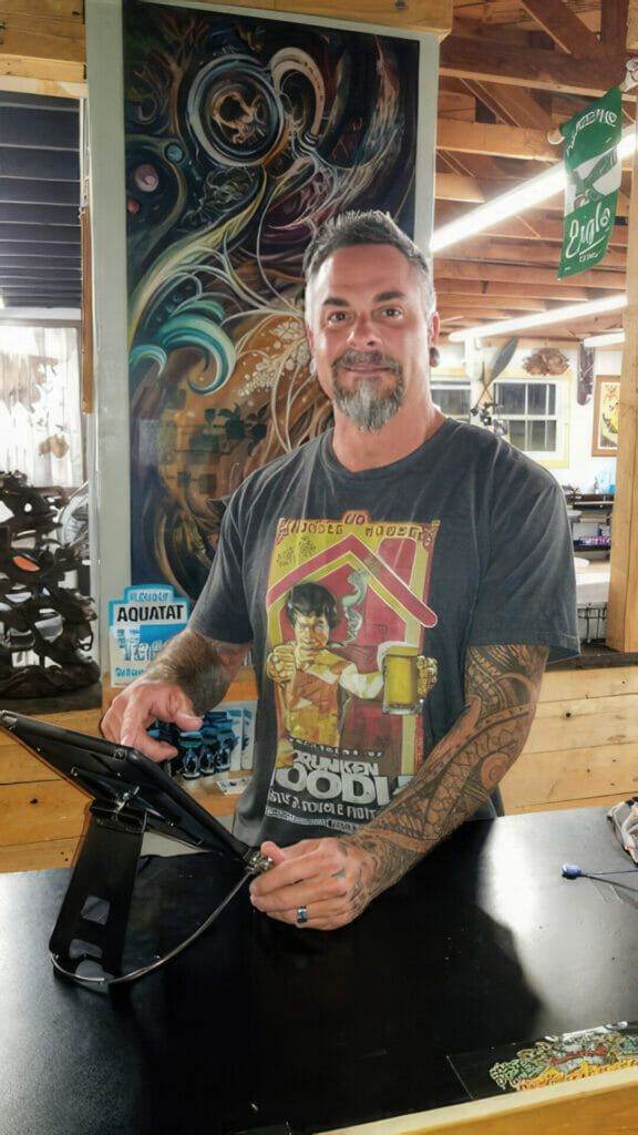 A man with tattoos working at a funhouse-like tattoo shop in San Diego.