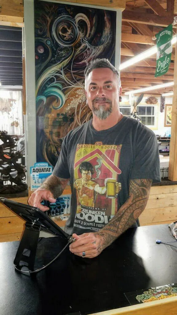A man with tattoos working at a funhouse-like tattoo shop in San Diego.