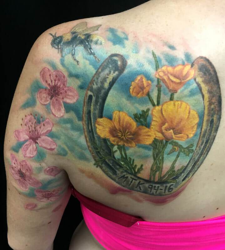 A woman's back with a horseshoe tattoo and flowers.