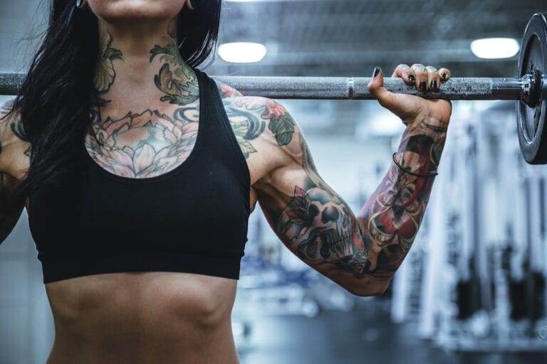 A woman with tattoos lifting a barbell in a gym.