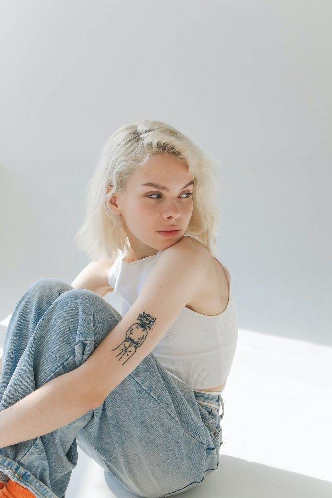 A woman with a full sleeve tattoo of small symbols sitting on the floor, showcasing incredible artistry.