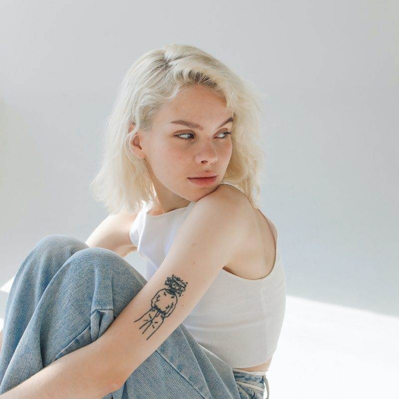 A woman with a full sleeve tattoo of small symbols sitting on the floor, showcasing incredible artistry.