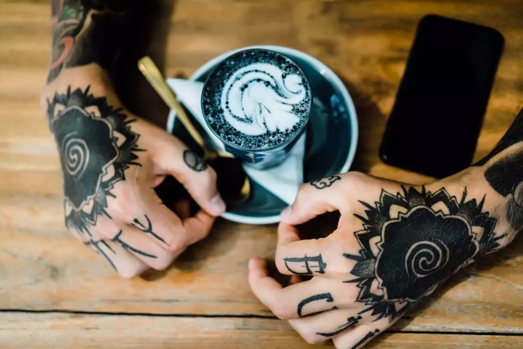 A man with transforming tattoos holding a cup of coffee.