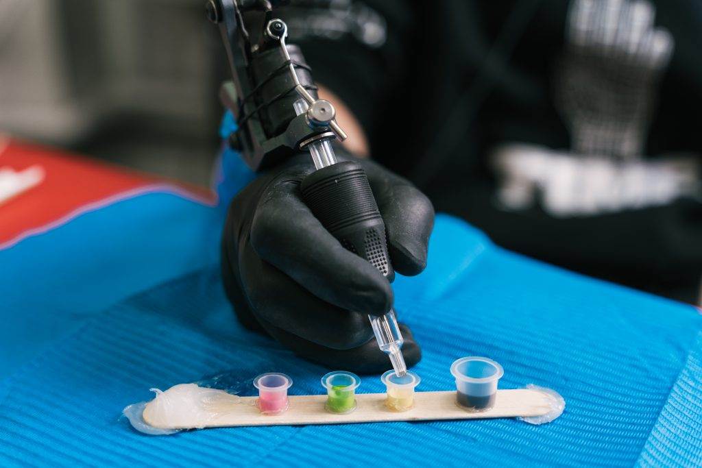 A person in black gloves using a tattoo gun to create a beautiful design on someone's skin.