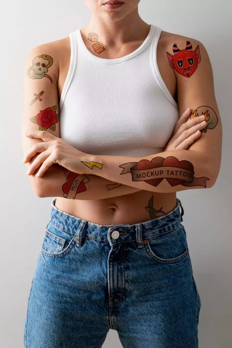 Person in a white tank top and jeans with colorful Funhouse Tattoo mockup designs on their arms, including a devil, skull, rose, and lightning bolt, standing with crossed arms in San Diego.