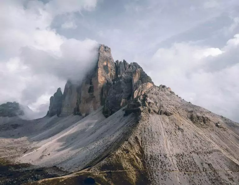 A rugged mountain peak partially shrouded in clouds, reminiscent of a San Diego tattoo design, with rocky slopes leading down to a sparse, arid landscape.