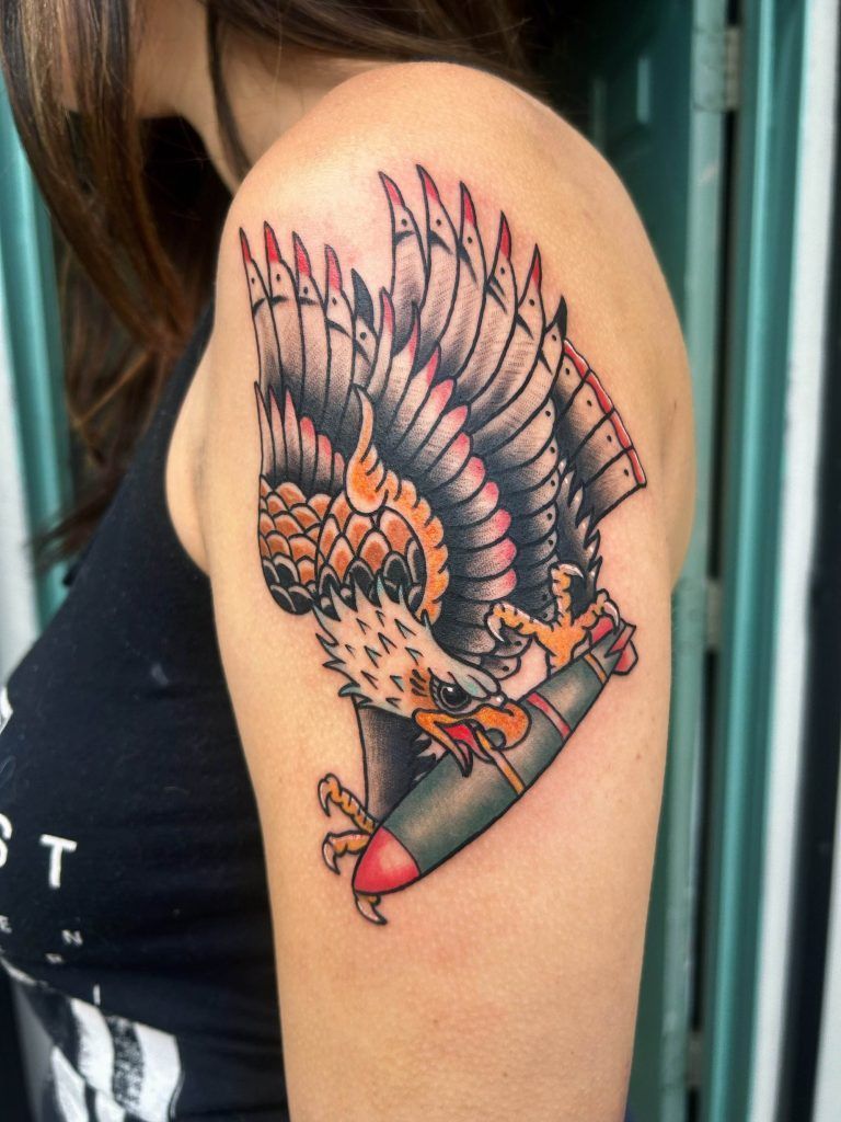 A tattoo of an eagle clutching a bomb is displayed on an individual's upper arm.