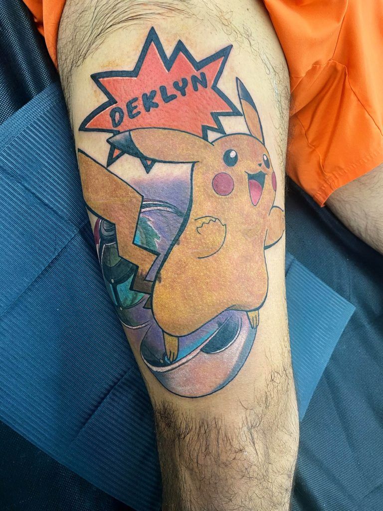 A colorful tattoo featuring Pikachu with a speech bubble containing the name "DEKLYN" on a person's leg.