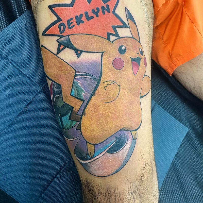 A colorful tattoo featuring Pikachu with a speech bubble containing the name "DEKLYN" on a person's leg.