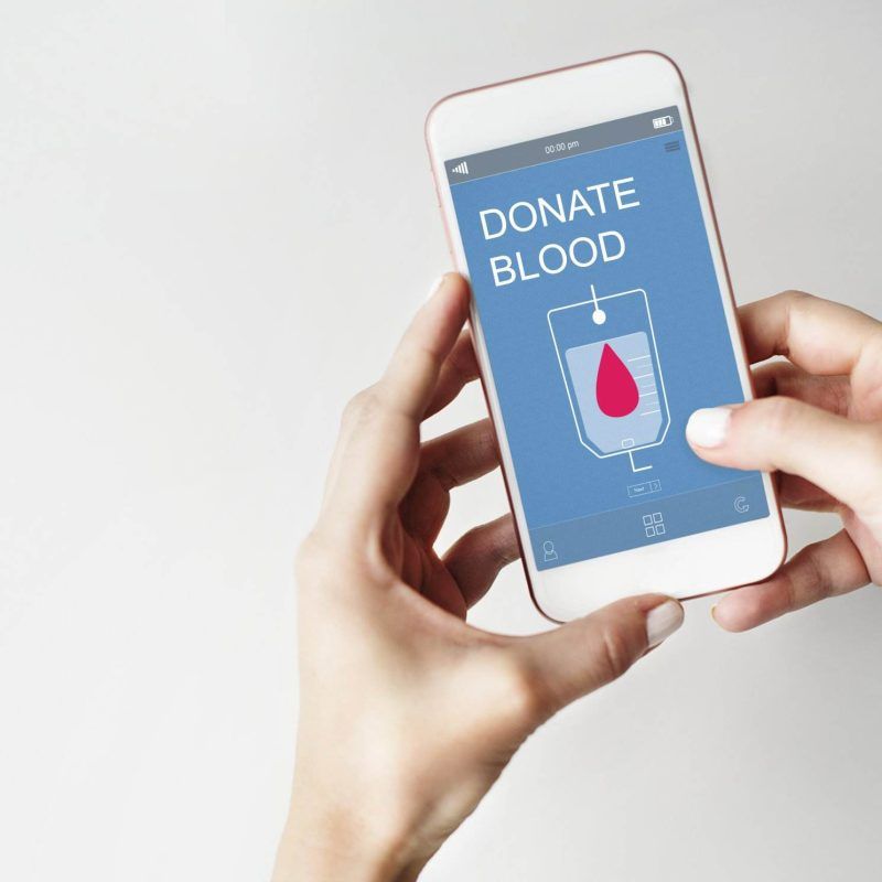 A person with a vibrant tattoo holds a smartphone displaying a "Donate Blood" app screen, ready to make an impact.