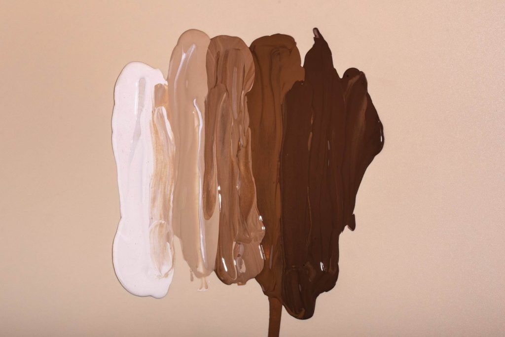 Five vertical swatches of foundation in varying shades from light to dark, applied on a beige background, showcasing the essence of Ink Perfection.