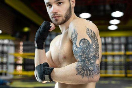 A man with boxing gloves and arm tattoos stands confidently in a gym, embodying the dedication and resilience of top athletes.