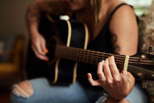 Someone passionately playing an acoustic guitar, focusing intently on the hand navigating the fretboard, as if each note were guided by unseen voices whispering through sound wave tattoos.