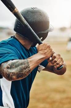 A baseball player in a blue jersey and helmet, gripping a bat with focused intensity, showcases the dedication of sports athletes. As he prepares to swing, the hint of tattoos on his arms reflects his unique personality and adds to his performance impact on the field.