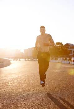 Shirtless man with tattoos jogging on a sunlit road, evoking the dedicated spirit of sports athletes, with buildings and trees elegantly lining the background.