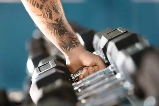 A tattooed arm, embodying an active lifestyle, grips a dumbbell from the rack.