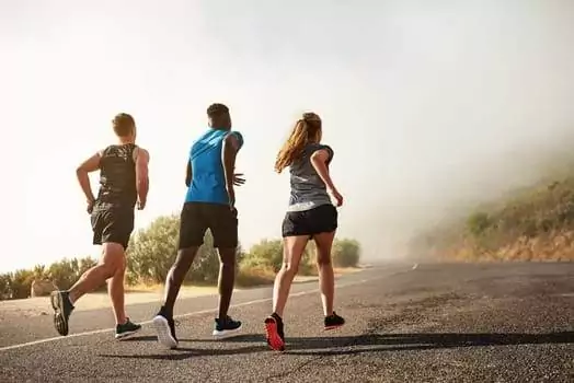 Three people embracing active lifestyles run on a paved road, with mist and foliage painting the background in serenity.