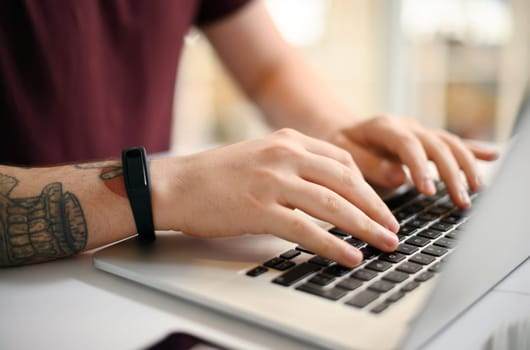 A person immersed in Silicon Valley vibes types on a laptop, their tattooed arm showcasing the vibrant tattoo culture, while a sleek fitness tracker adds a touch of tech industry flair.
