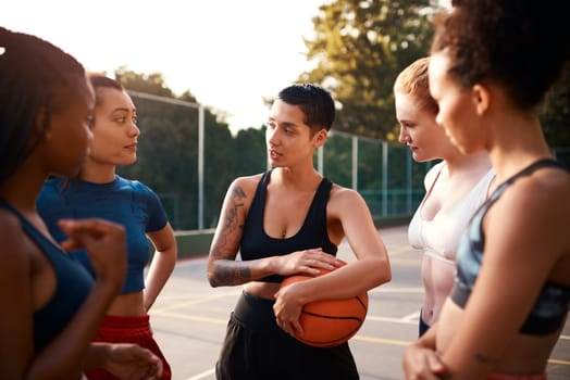 A group of sports athletes stand on a basketball court, engaged in conversation, with one holding a basketball. The tattoos peeking from beneath their uniforms hint at stories and motivations that impact their performance on and off the court.
