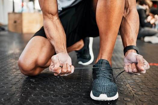 Kneeling on the gym floor, a person ties the laces of a black athletic shoe, embodying active lifestyles while mindful of tattoo guidelines.