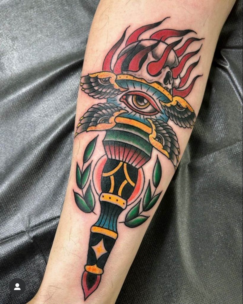 Colorful tattoo of a torch with an eye, wings, and flames on a forearm.