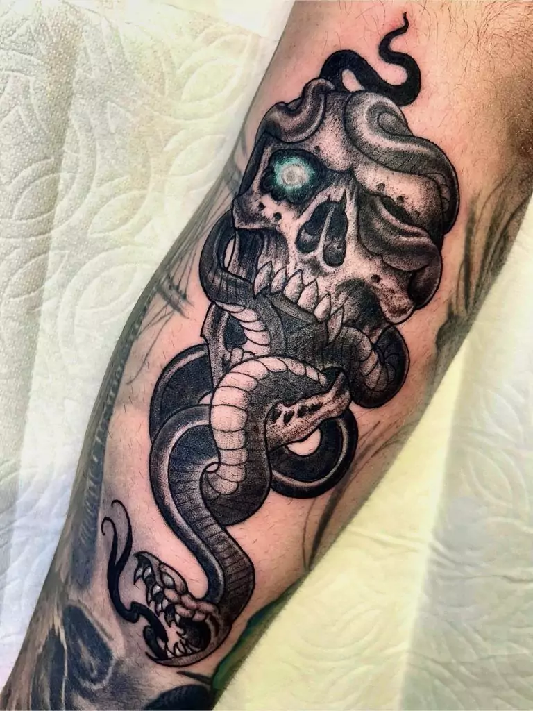Tattoo depicting a skull entwined with a snake, featuring a glowing eye, on a person's limb.