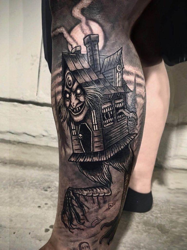 Tattoo of a witch's house with legs and a grinning face, located on a person's leg.