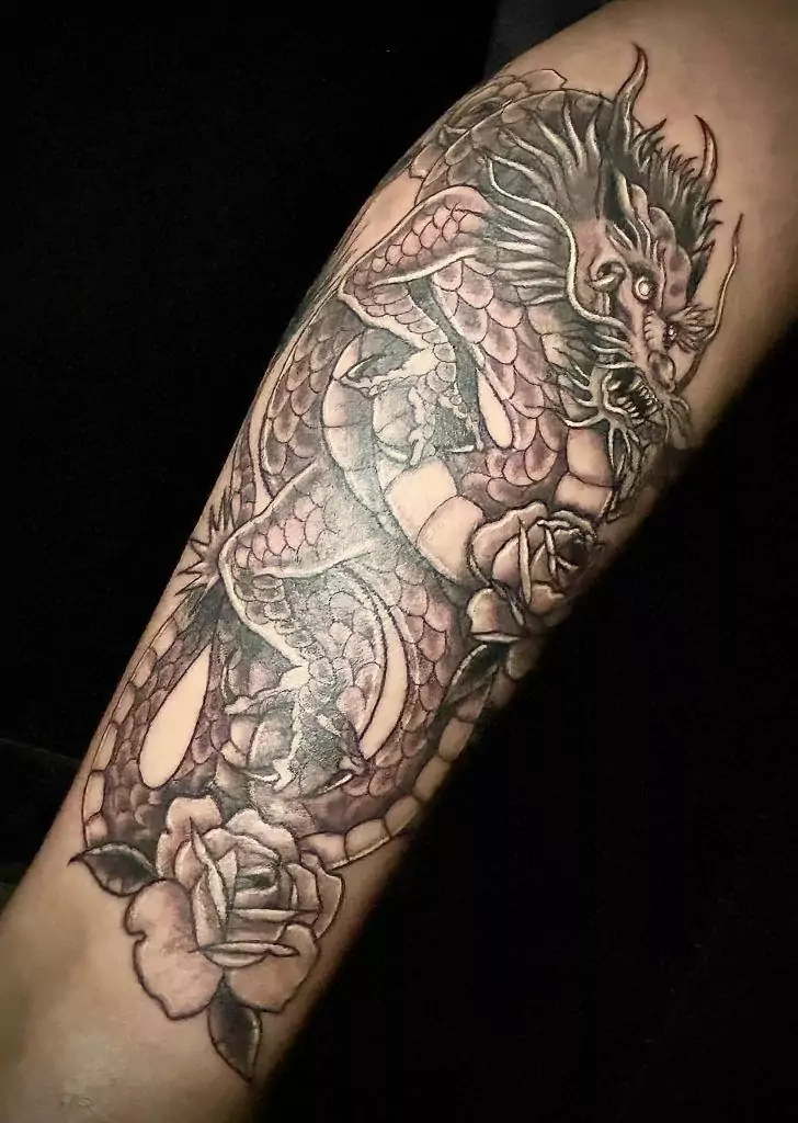 Intricate dragon tattoo with roses on a person's forearm, featuring detailed scales and fierce facial expression.