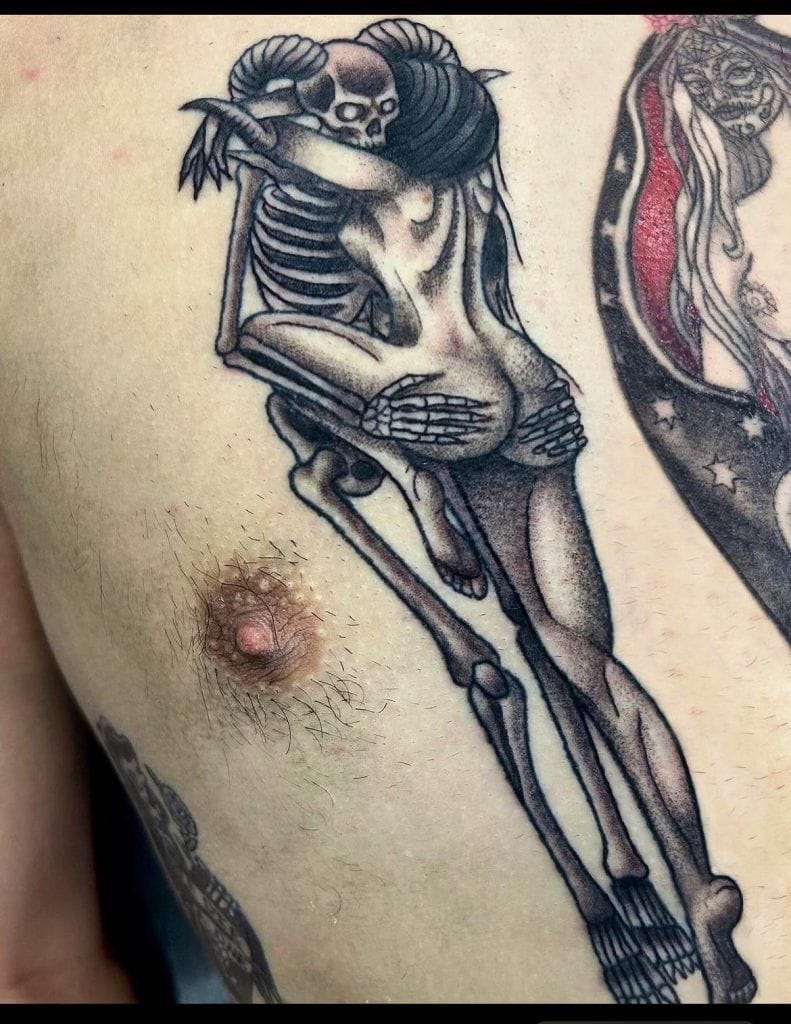 Tattoo of two skeletons embracing, one with long hair, on a person's skin.