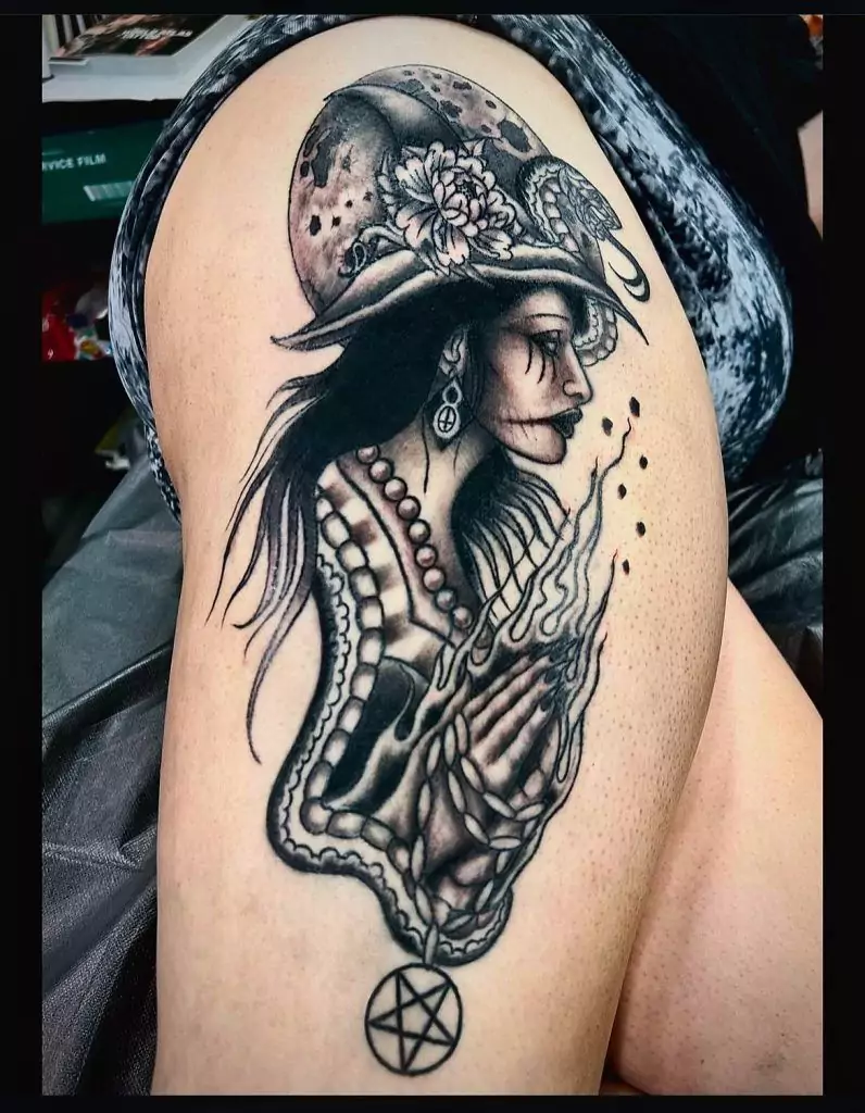 Tattoo of a woman in a hat, with long hair, flowers, and prayer hands, cover a person's upper arm. A skull and pentagram are also incorporated into the design.