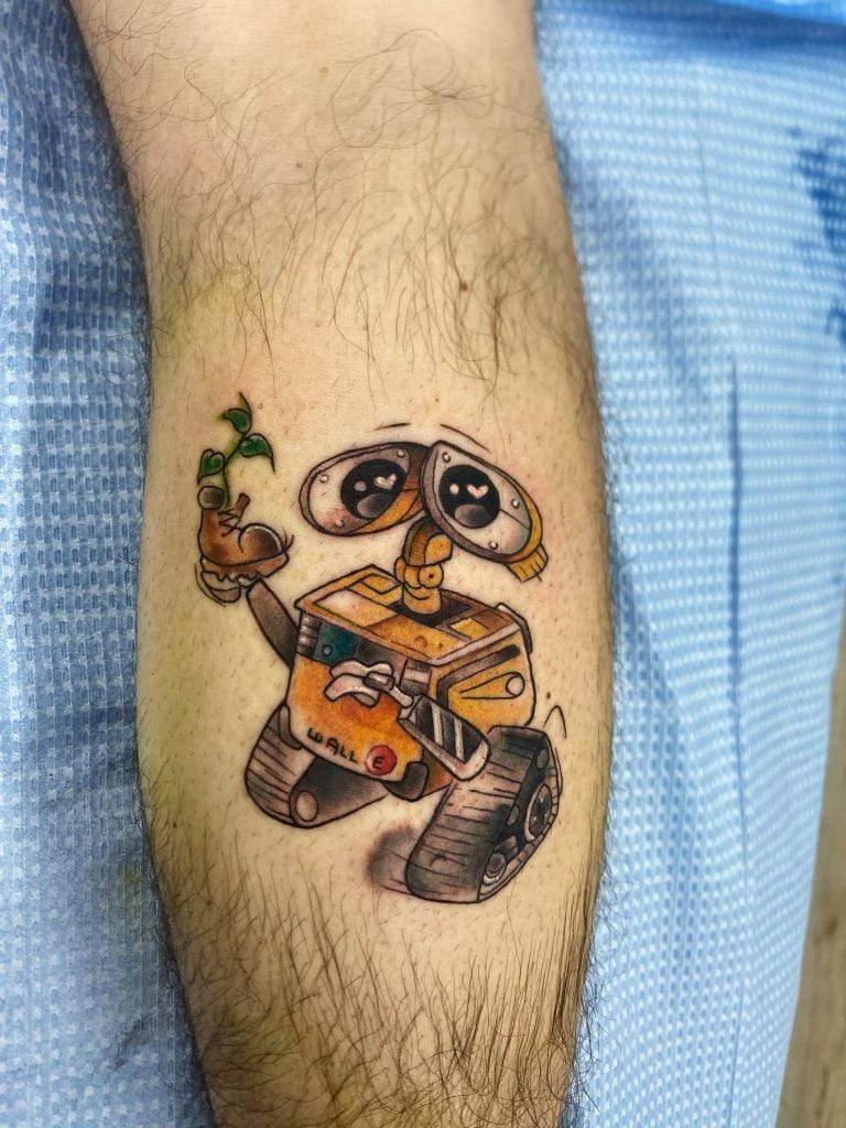 Tattoo of a small robot holding a plant on a person's arm, wearing a blue garment.
