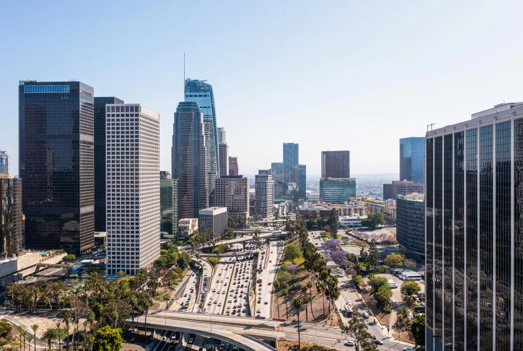 Aerial view of downtown Los Angeles with tall office buildings, a busy freeway, and clear skies in the background—a perfect contrast to San Diego tattoo culture and the rich tattoo history found along California’s coast.