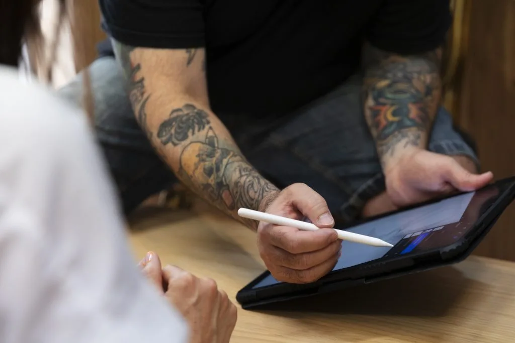 Person with colorful tattoos on arms using a stylus on a tablet screen.