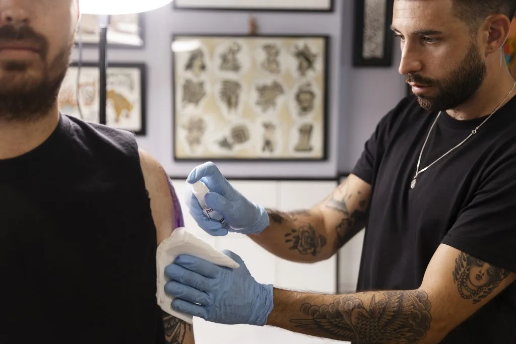 Tattoo artist administering a tattoo to a persons upper arm in a studio.