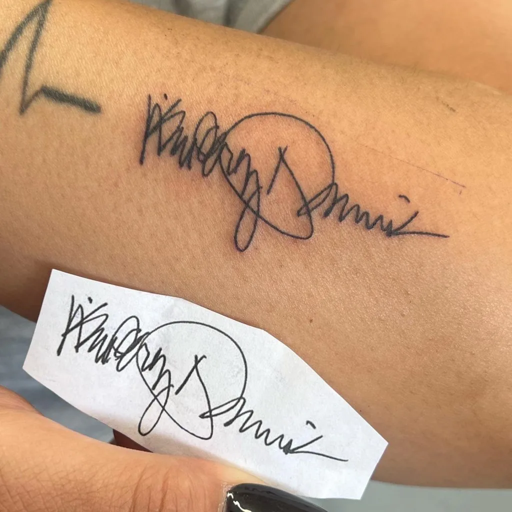 Tattoo of a signature with a circle around part of the name on a persons arm.