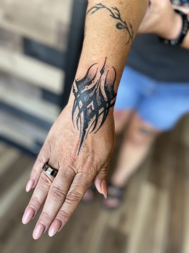 Black tribal-style tattoo on wrist and forearm, with a small branch and leaf above.