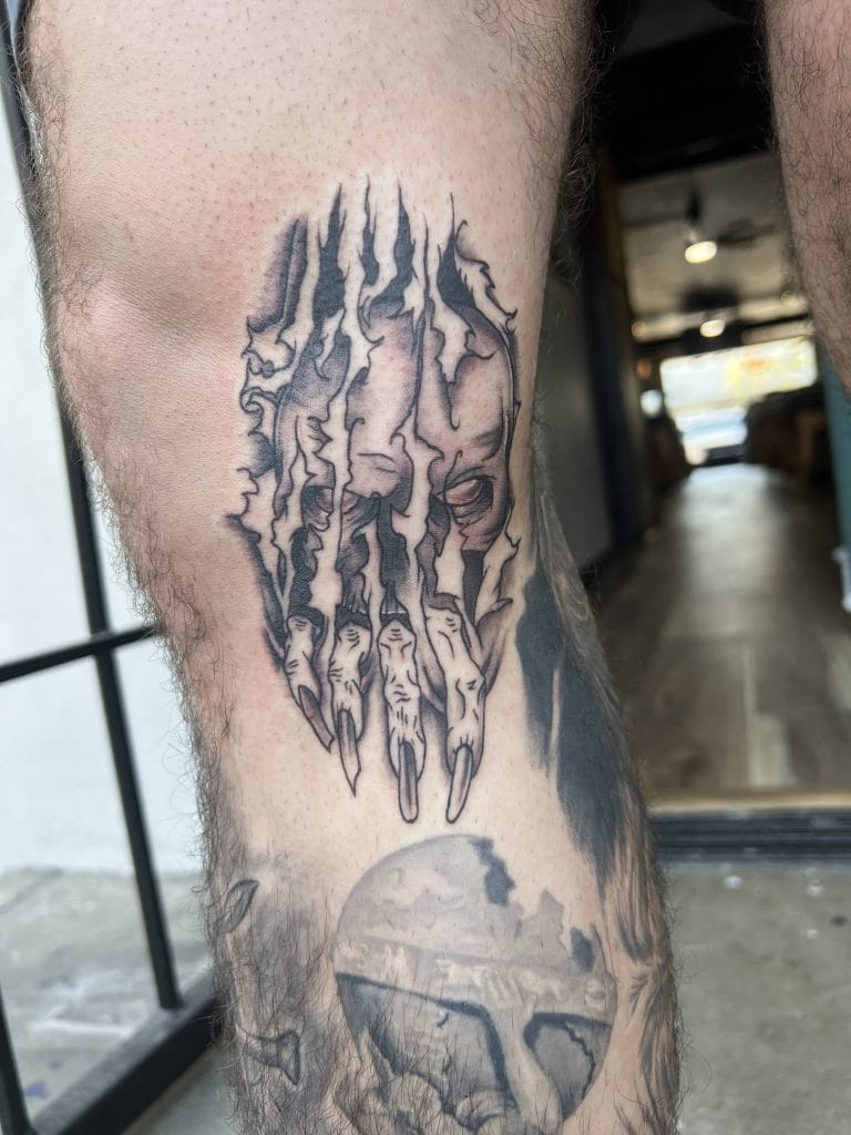 Tattoo of a distorted face with elongated fingers above a skull on a persons arm.