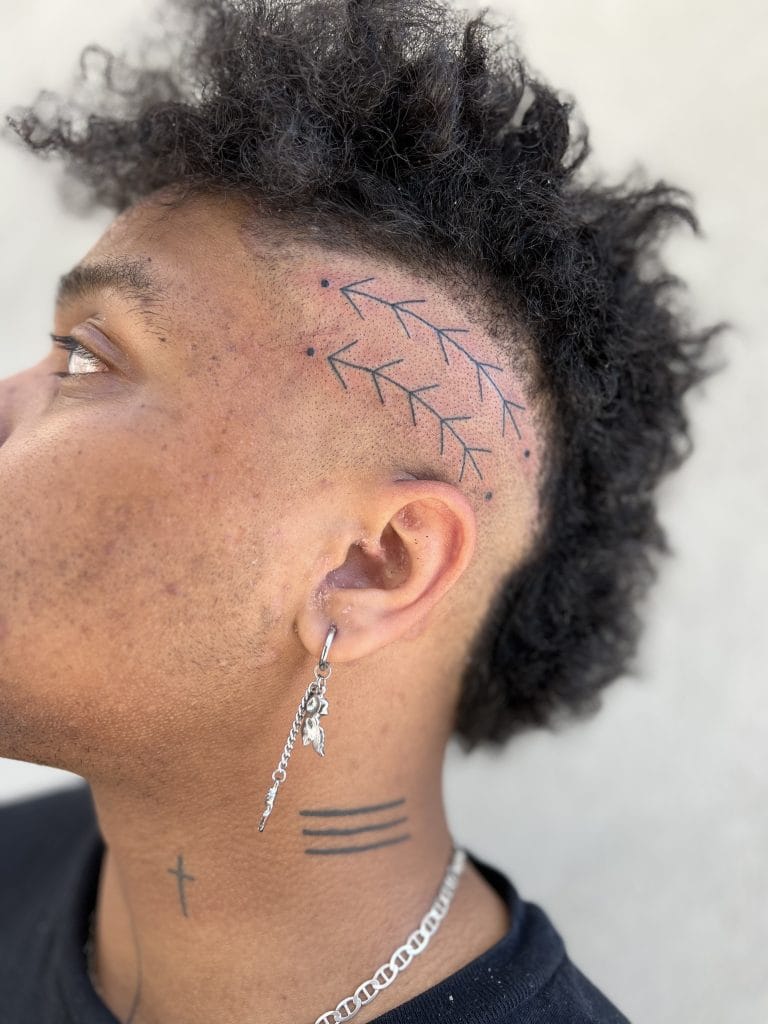 Side profile of a person with a branch tattoo on the scalp, three lines tattoo on the neck, and a cross tattoo on the neck.