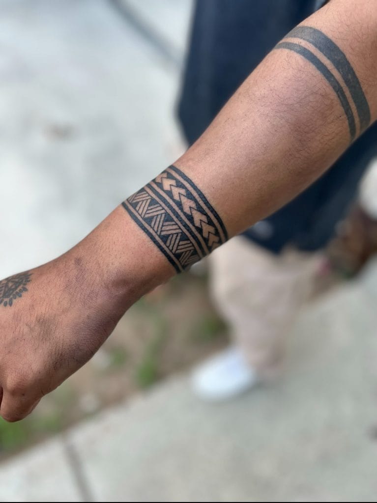 Forearm with multiple black geometric tattoos, including bands and intricate patterns.