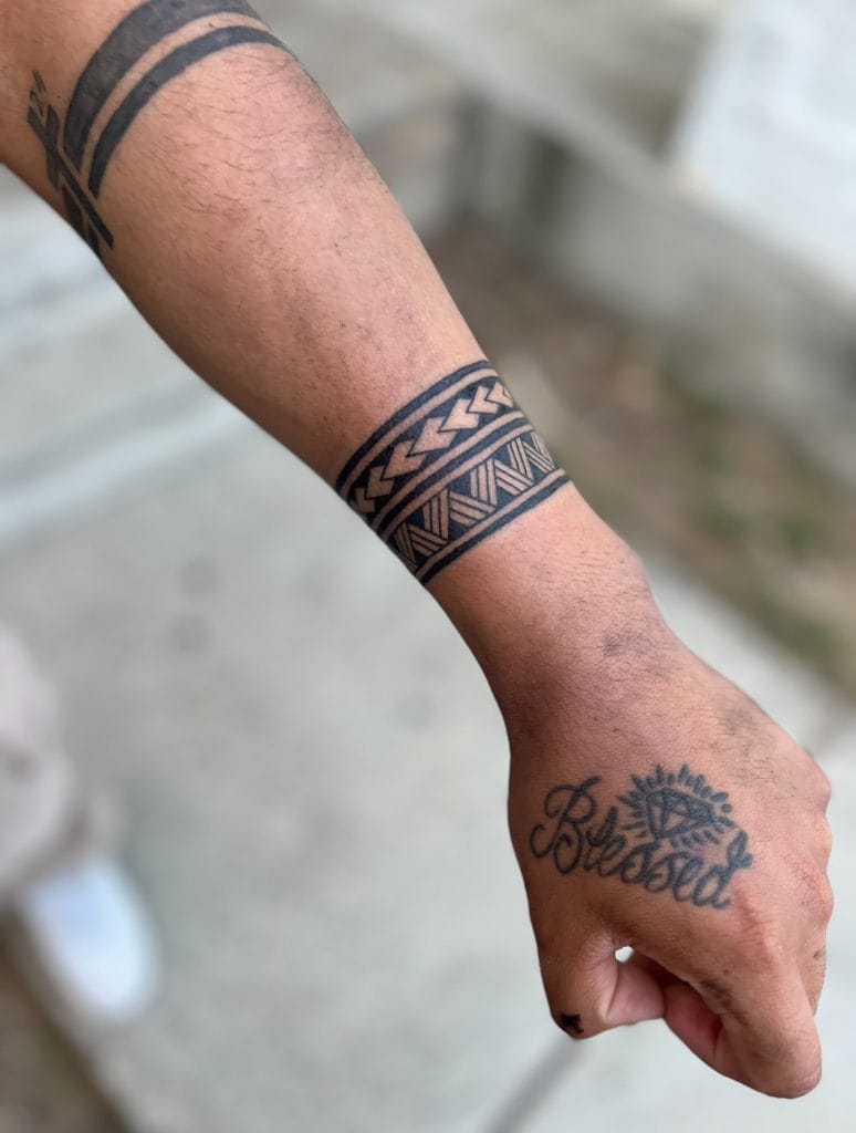 Tattoo of the word Blessed with a sun and diamond design on the hand, and geometric patterns on the forearm.