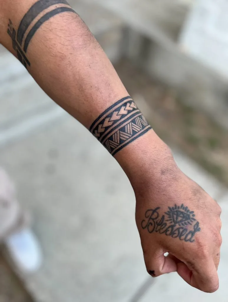 Tattoo of the word Blessed with a sun and diamond design on the hand, and geometric patterns on the forearm.