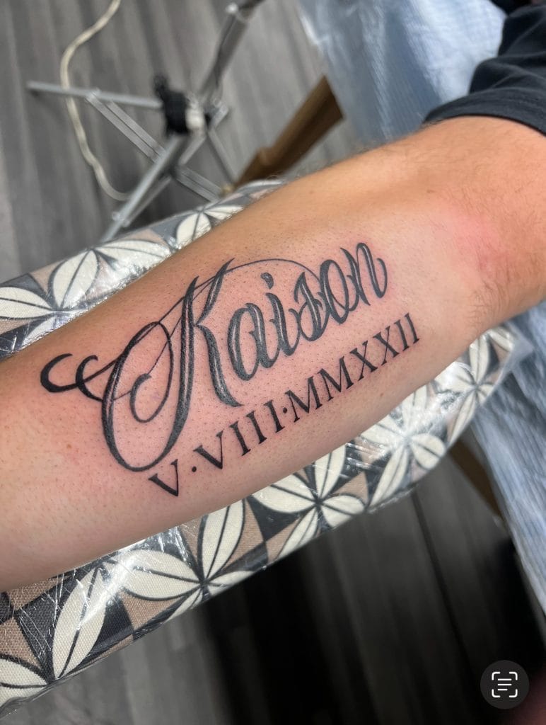 Tattoo of the name Kaizoh with Roman numerals V-VIII-MMXXII below, on forearm.